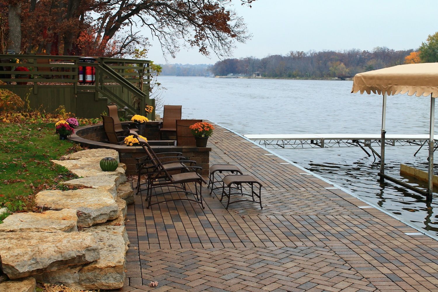 Brick patio by lake with seating, stone wall, and a covered boat dock.