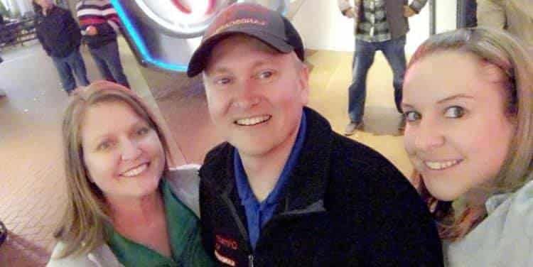 Three people smiling at the camera, posing for a selfie indoors.