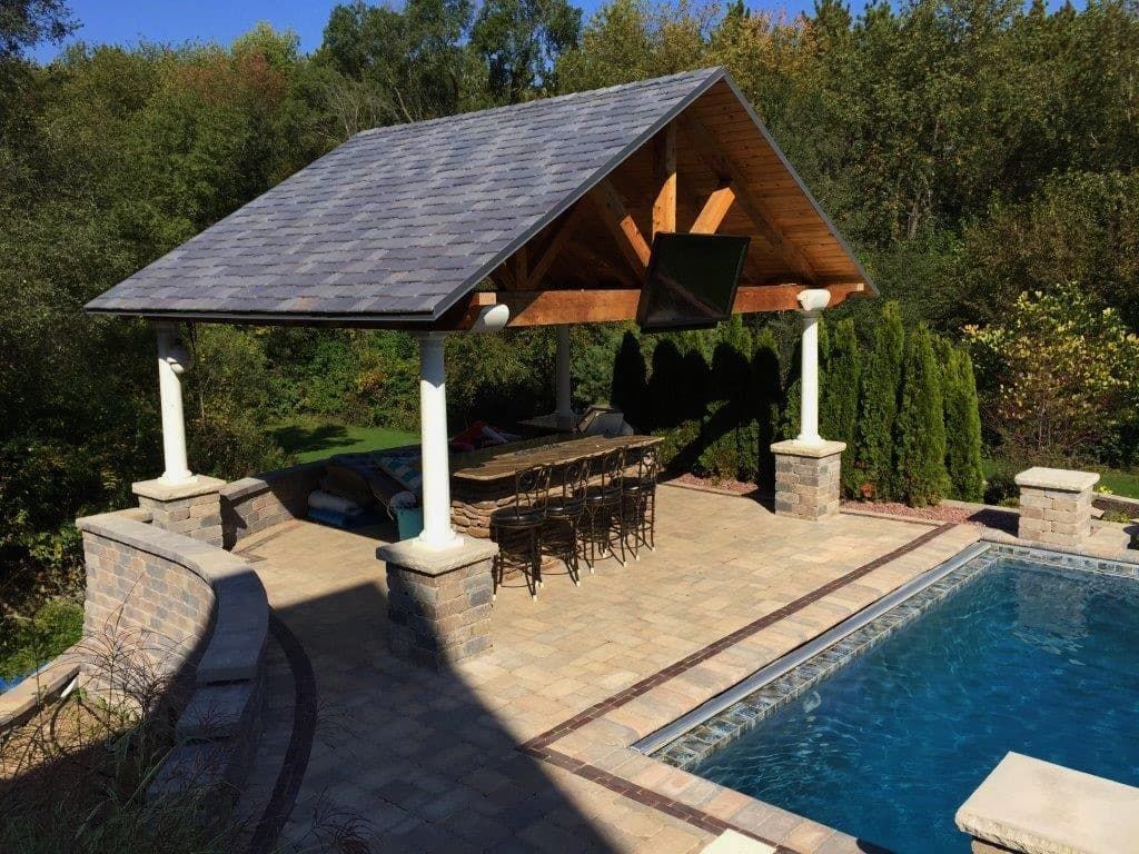 Poolside pavilion with bar, TV, and seating, overlooking a pool and surrounded by greenery.