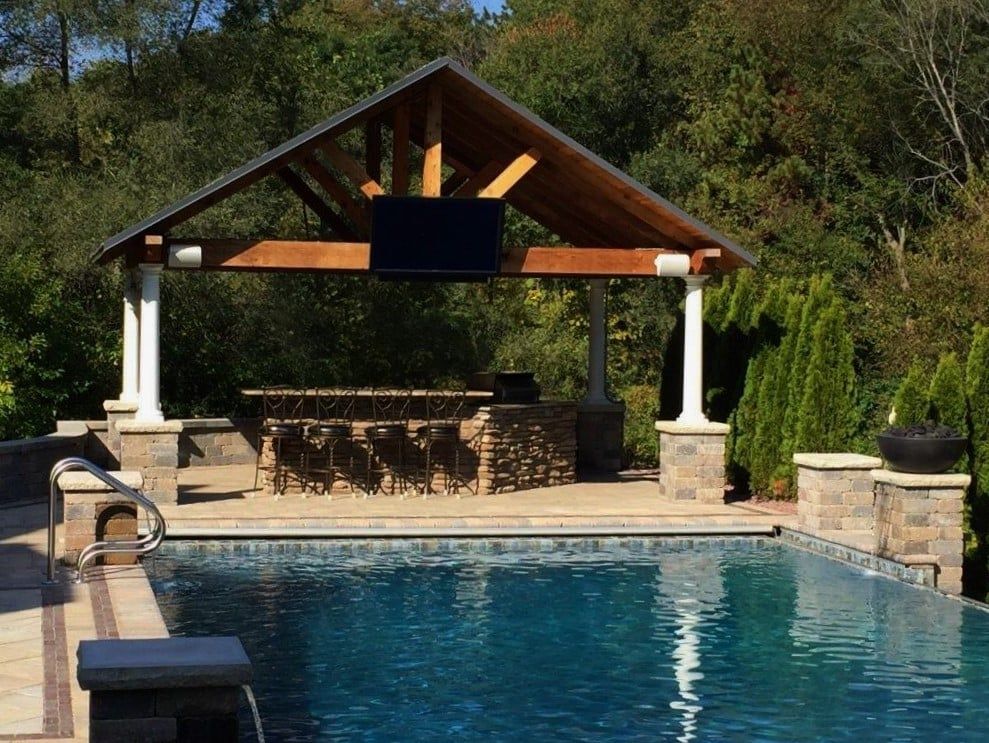 Poolside bar with a wooden roof, stone bar, and a television overlooking the pool.