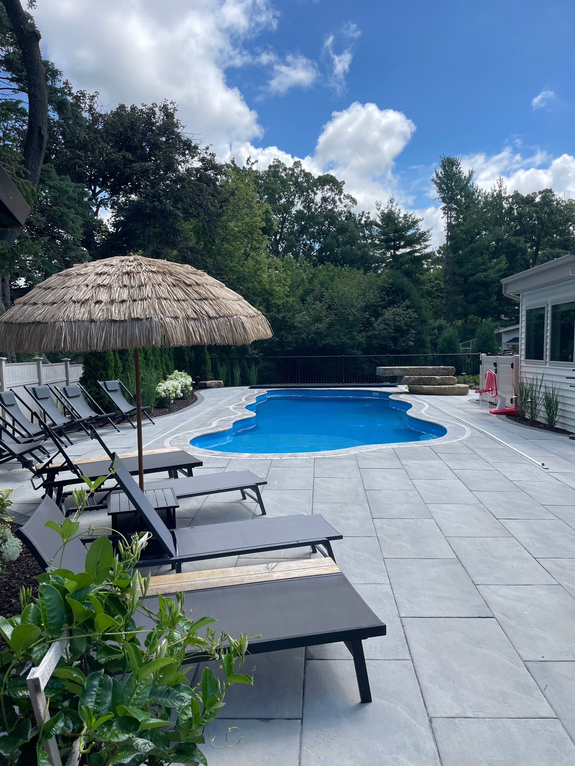 Pool area with blue water, grey lounge chairs, a thatched umbrella, and blue sky.