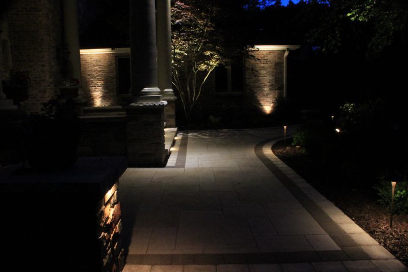 Pathway illuminated by outdoor lights at night, leading toward a building entrance.