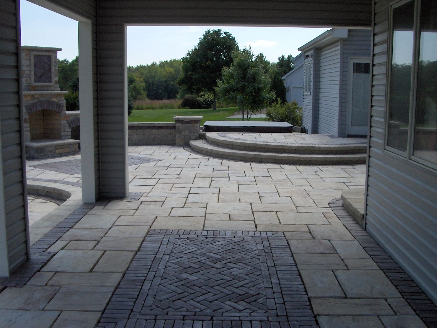 Outdoor patio with stone pavers, steps, and a fireplace framed by a covered porch.