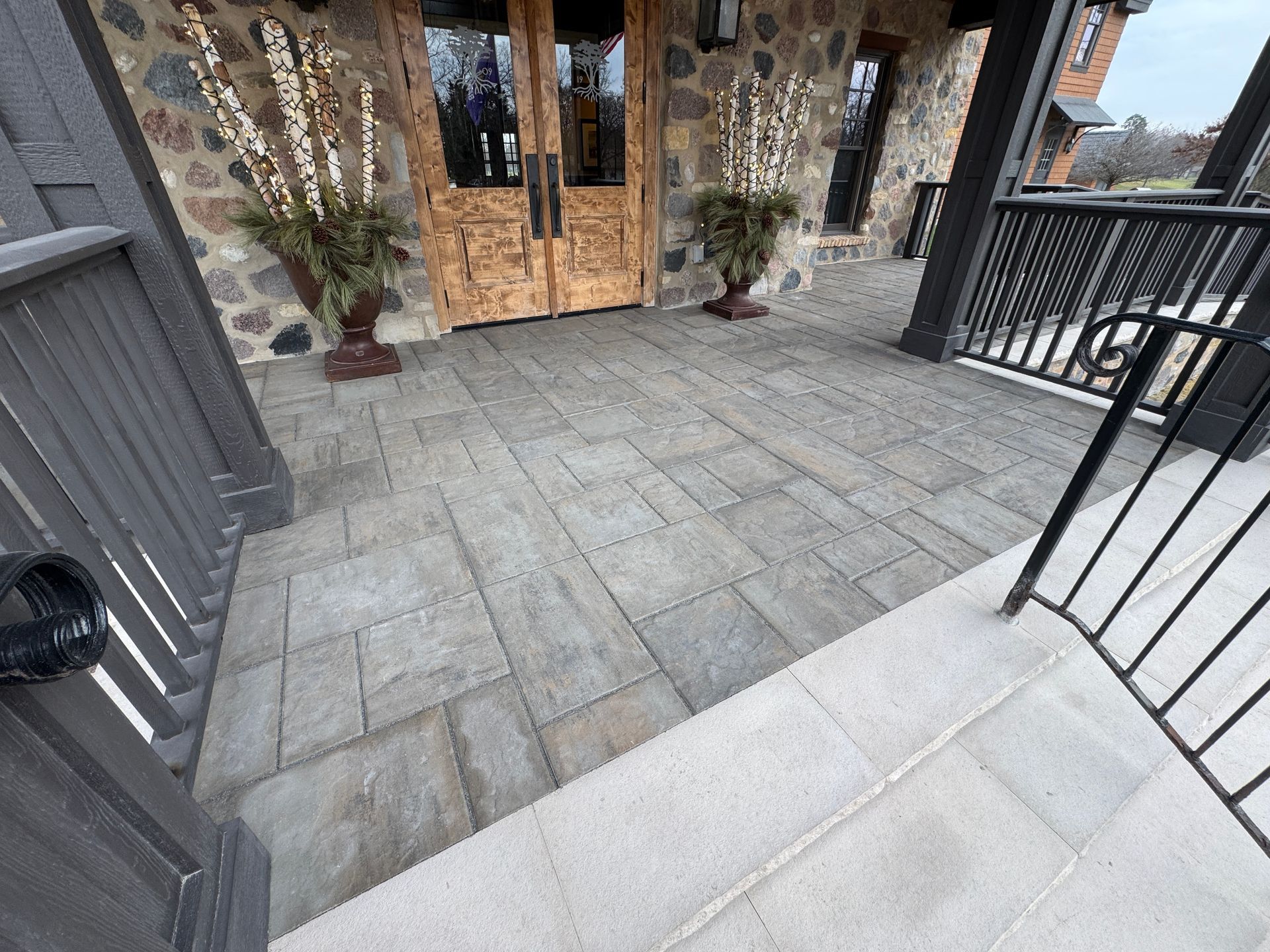Stone patio leading to wooden double doors of a stone building, two planters flanking the entrance.