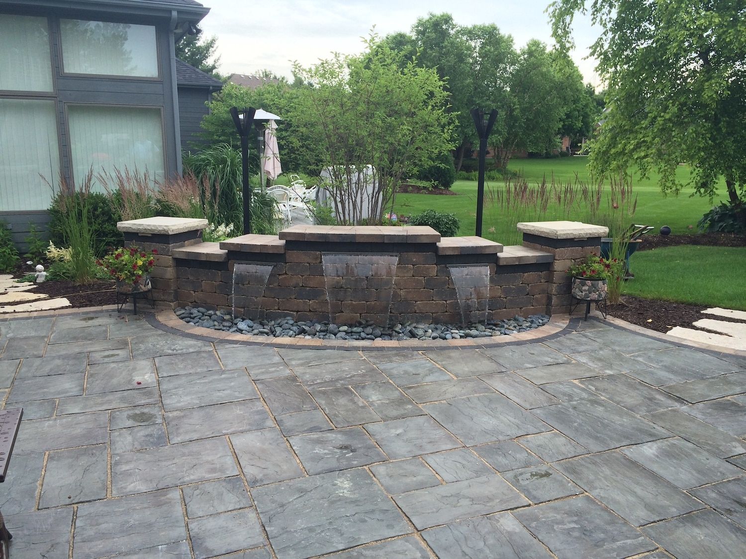 Patio with a brick water feature, stone pavers, and landscaped yard.
