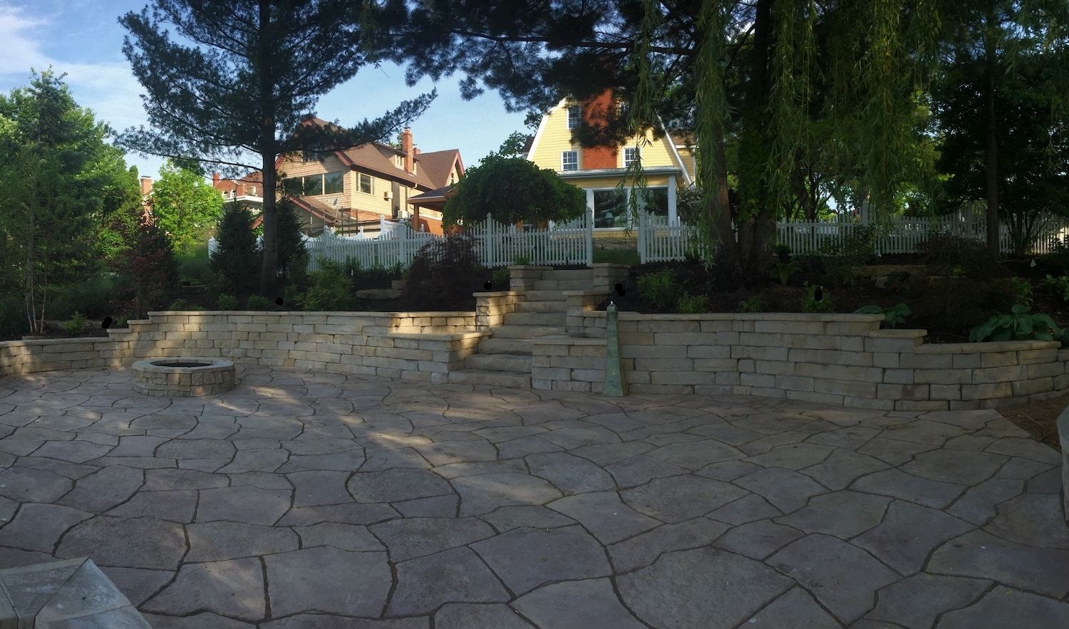 Stone patio with tiered retaining walls, stairs, and a view of houses and trees.