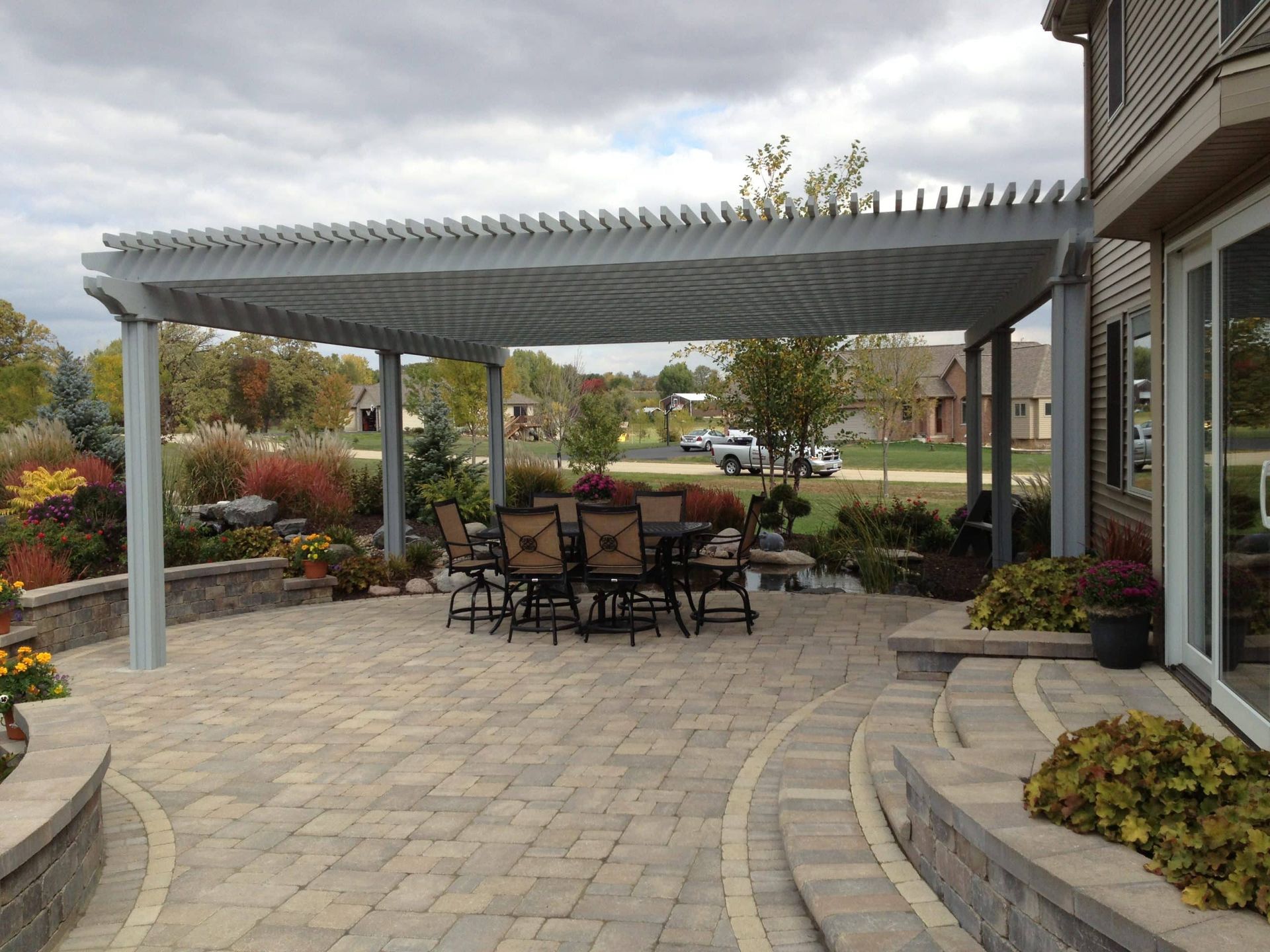 Patio with grey pergola over dining set, adjacent to a house with sliding glass doors.