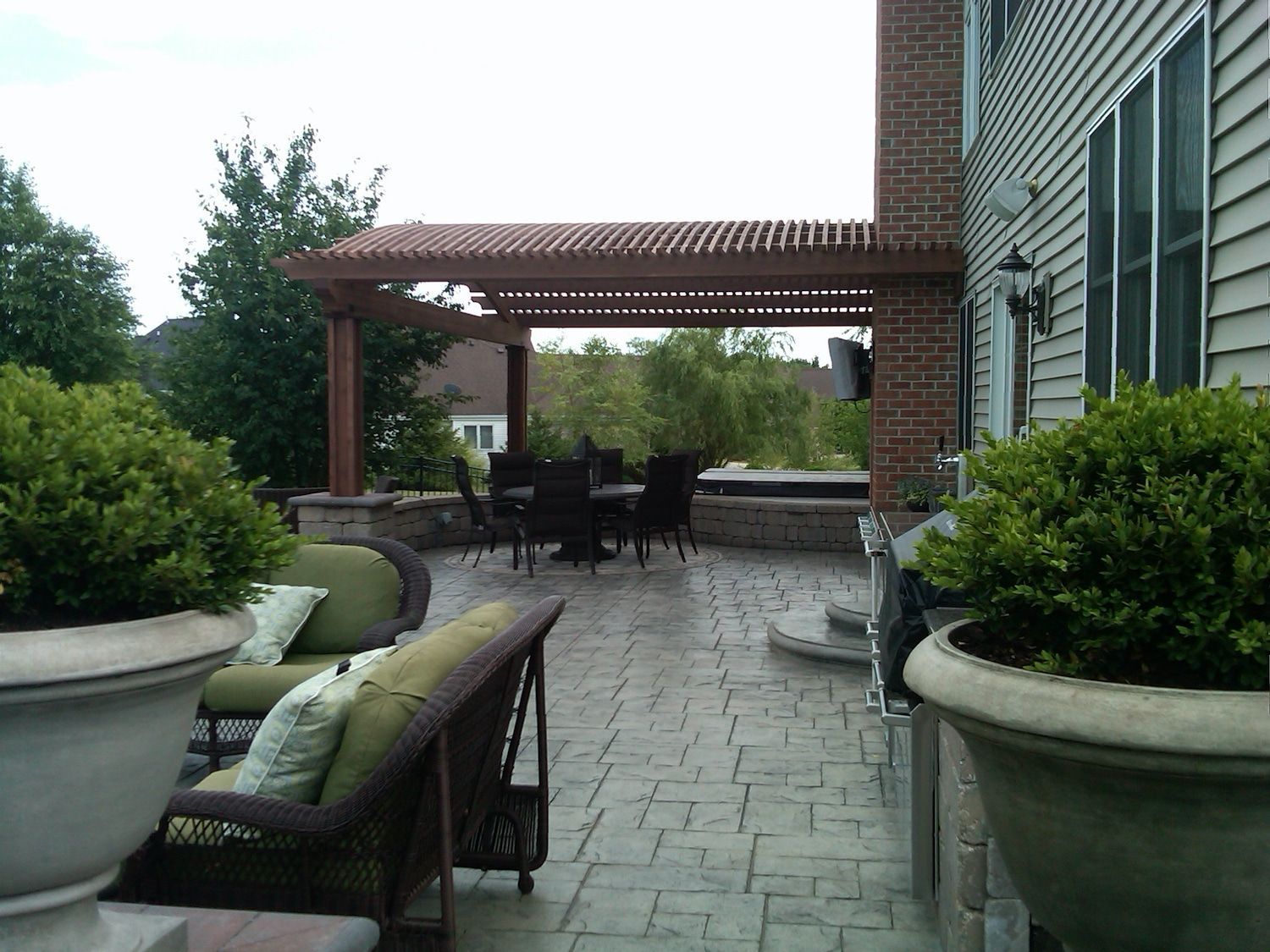 Patio with pergola, furniture, and landscaping, against a house with a brick chimney.