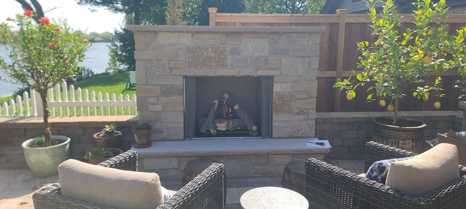 Outdoor fireplace with seating, potted trees, and a lake view.