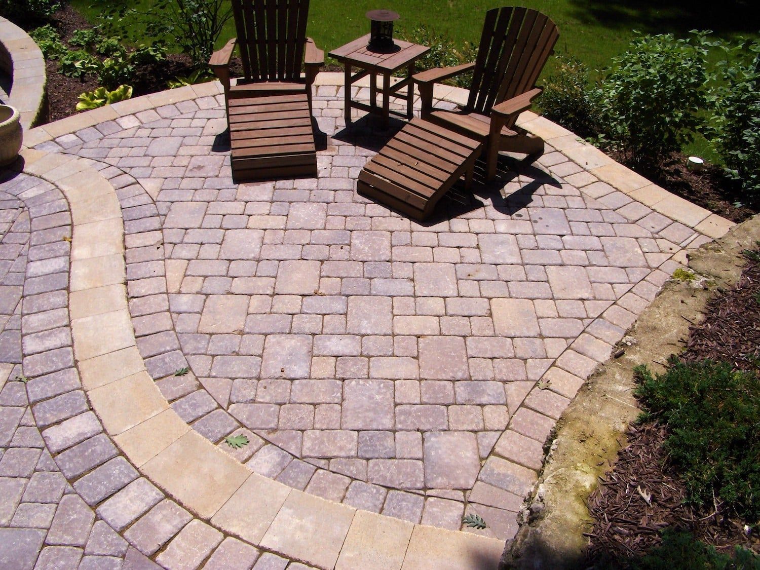 Paver patio with two wooden chairs, small table, and pathway.