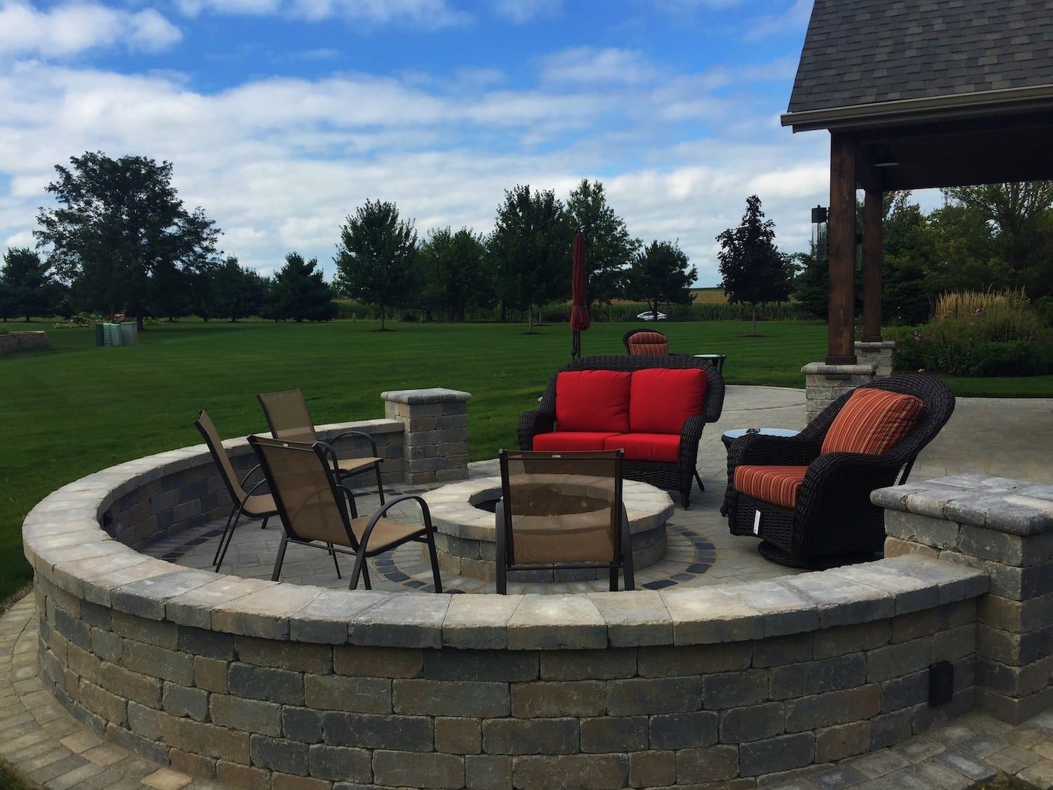 Fire pit with seating on a patio overlooking a grassy yard under a partly cloudy sky.
