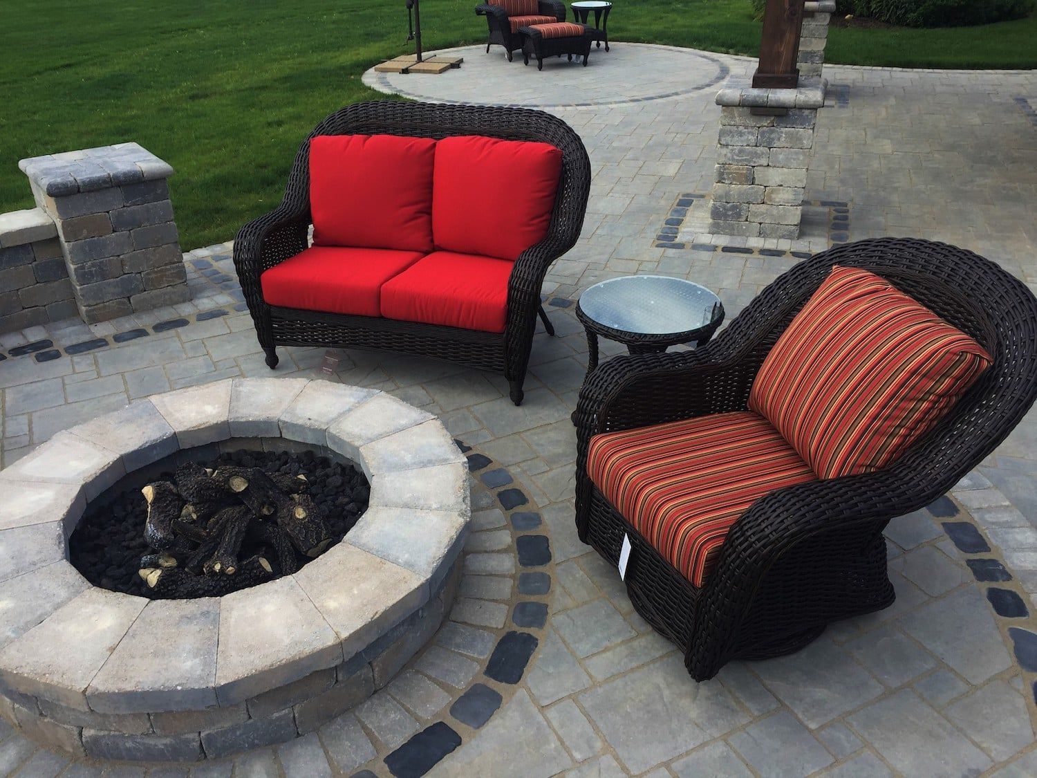 Patio furniture arrangement with a fire pit, including a loveseat with red cushions and an armchair with orange cushions.