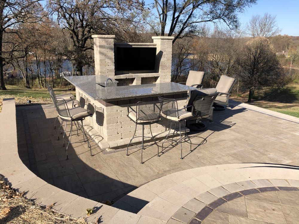 Outdoor kitchen with TV, bar seating, and view of a lake. Concrete construction with dark countertop.