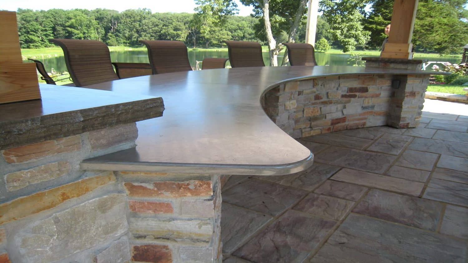 Outdoor bar with curved countertop, brick and stone base, overlooking a lake.