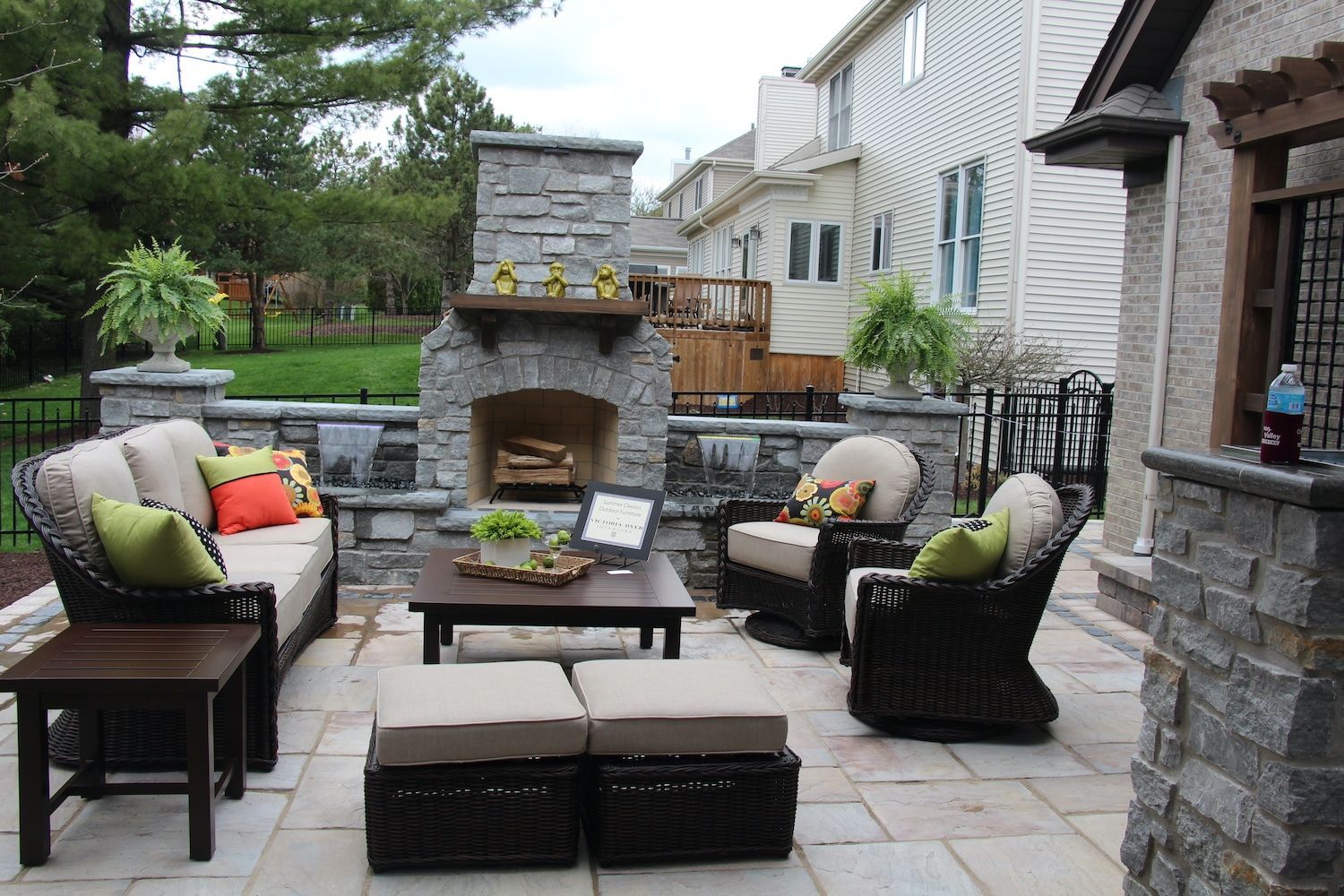 Patio with stone fireplace, seating, and lush greenery in a residential backyard.