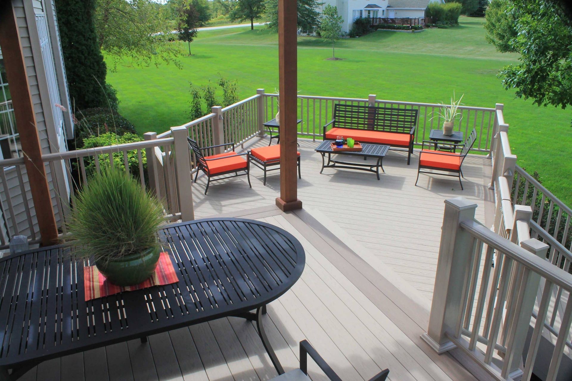 Outdoor deck with seating, overlooking green lawn. Orange cushions contrast with neutral deck.