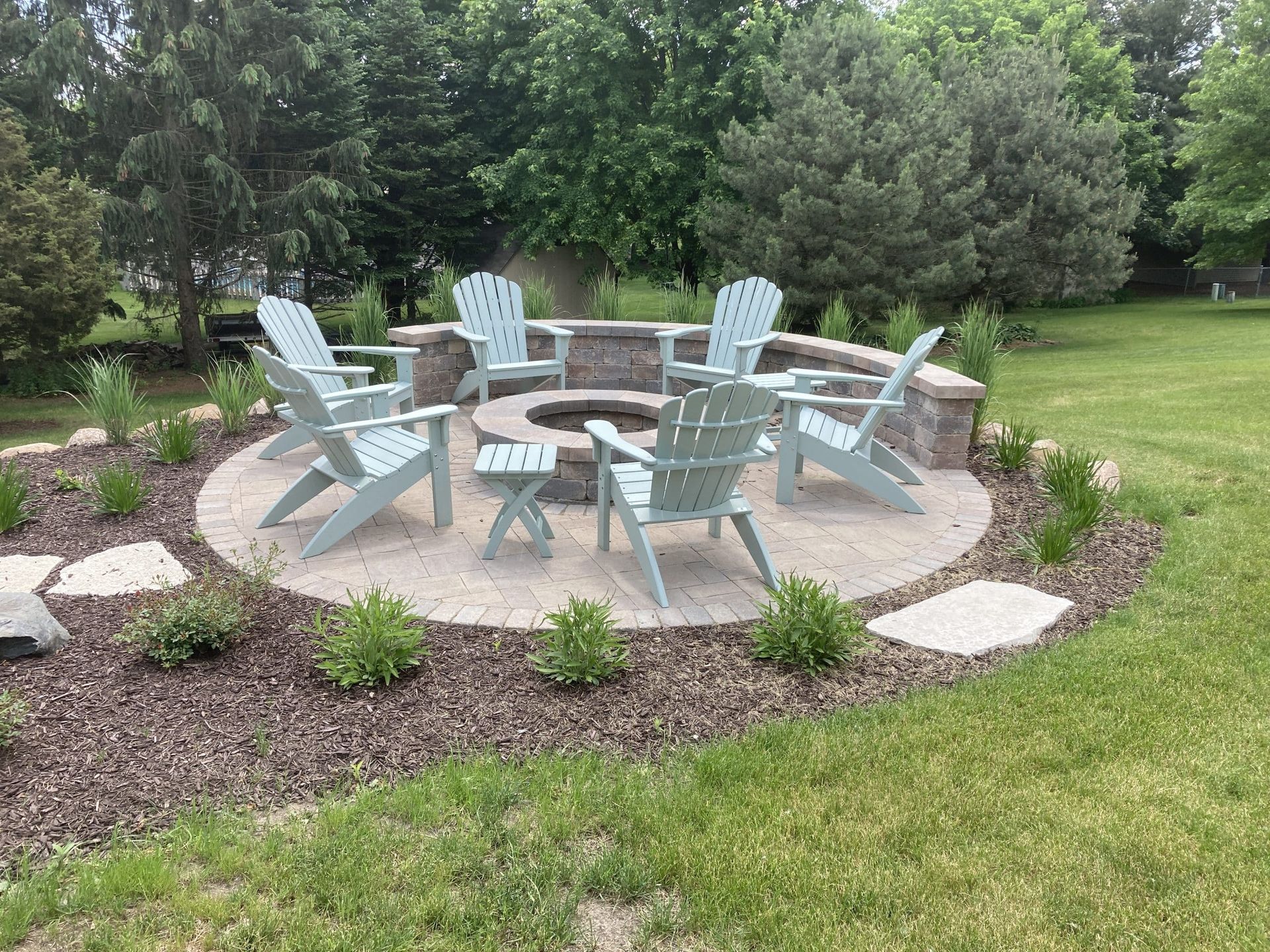 A fire pit with light blue Adirondack chairs arranged in a circle on a landscaped lawn.