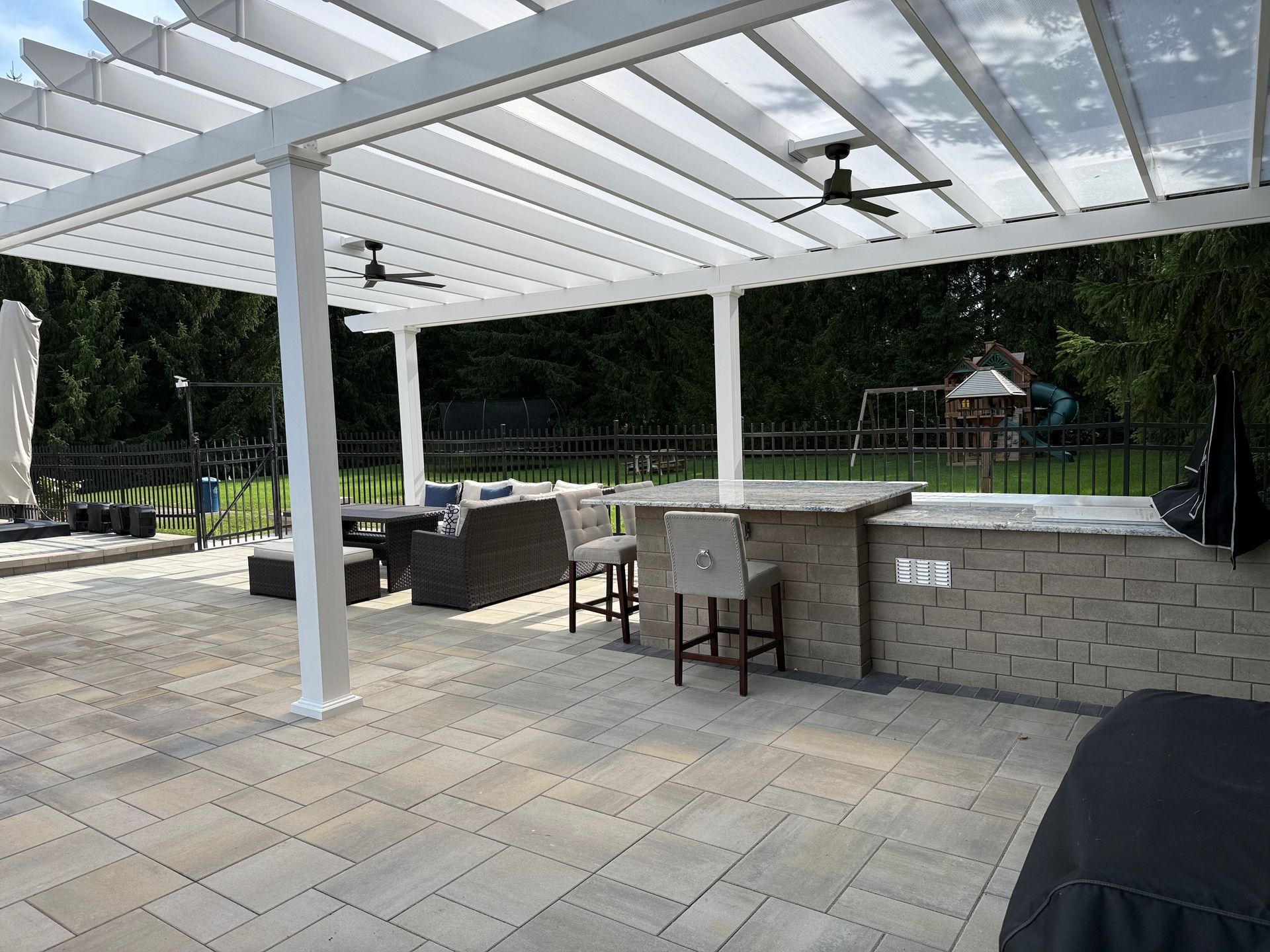 Patio with pergola, outdoor kitchen, seating area, and backyard playground.