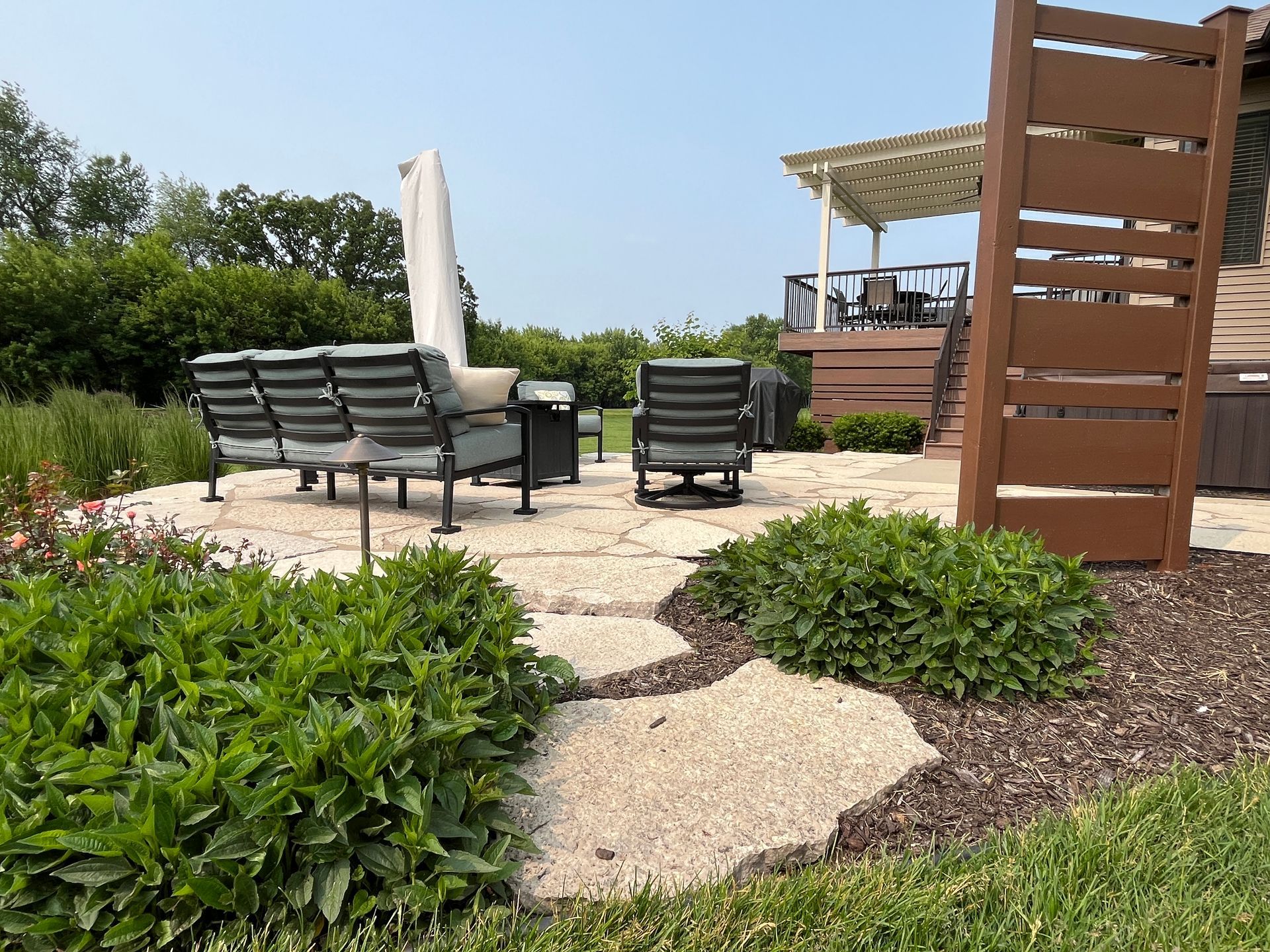 Patio with chairs, umbrella, and fire pit on stone pavers, with a wooden privacy screen.