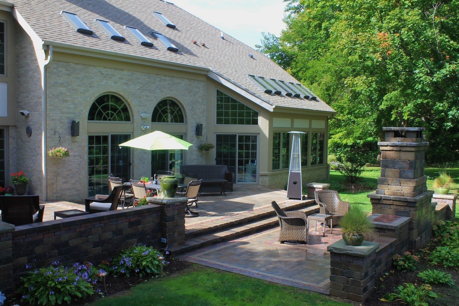 Patio with seating, umbrella, and a large house with arched windows and a brick chimney.