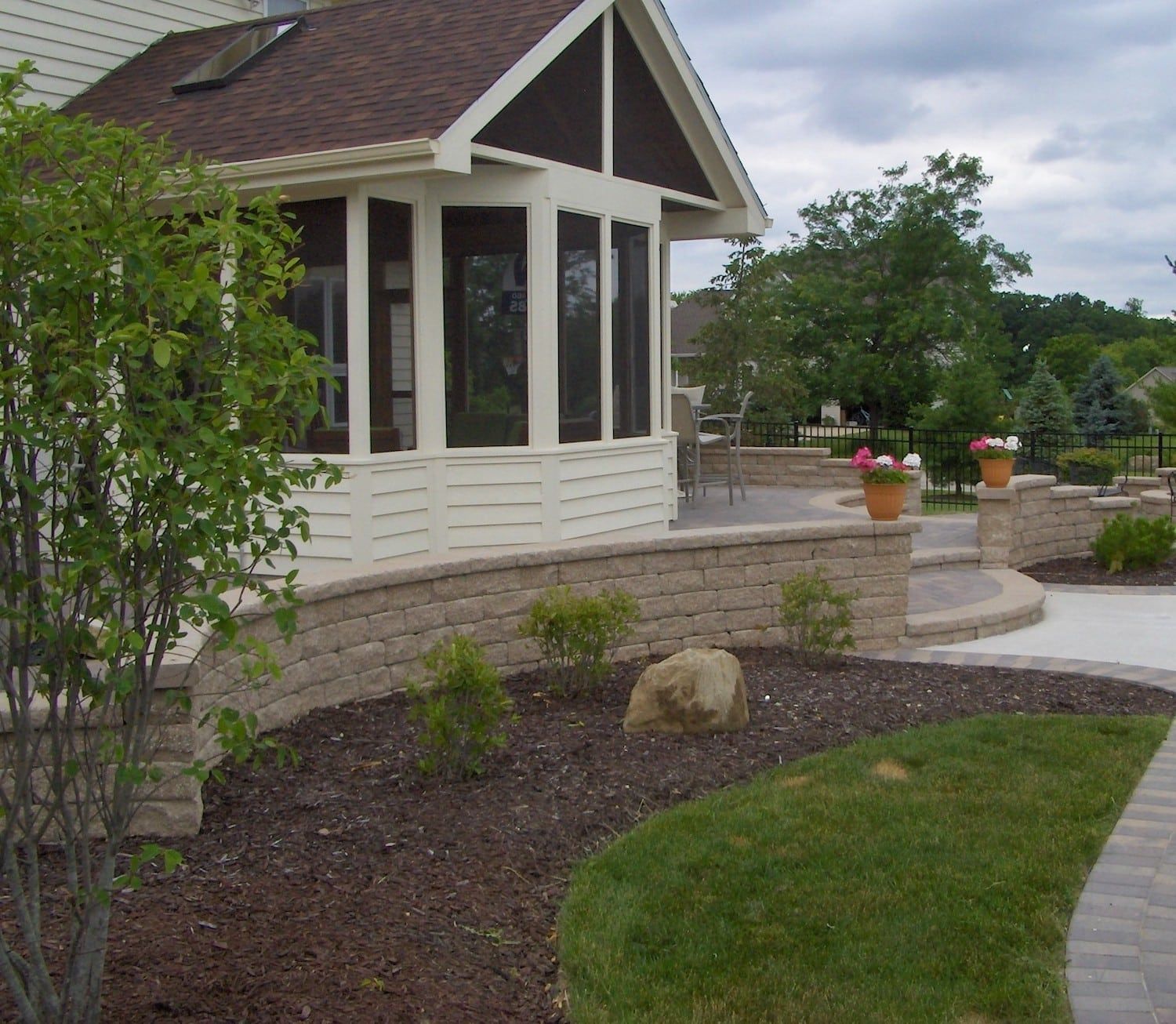 Stone patio with retaining walls and a screened-in porch under a cloudy sky.