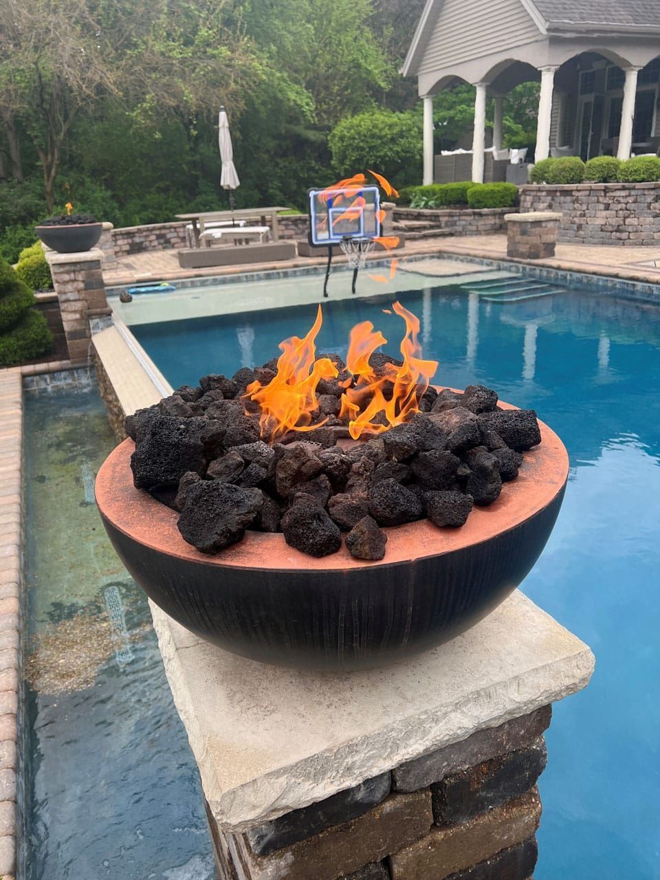Fire bowl with lava rocks burning next to a pool.