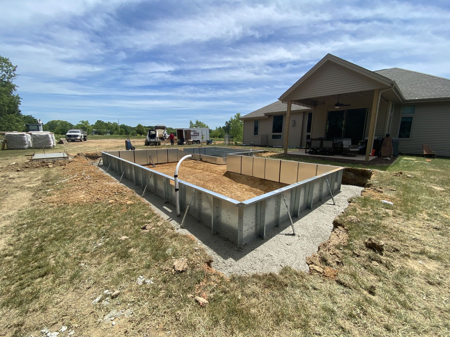 Pool construction: metal frame in yard near house, with dirt interior, cloudy sky overhead.