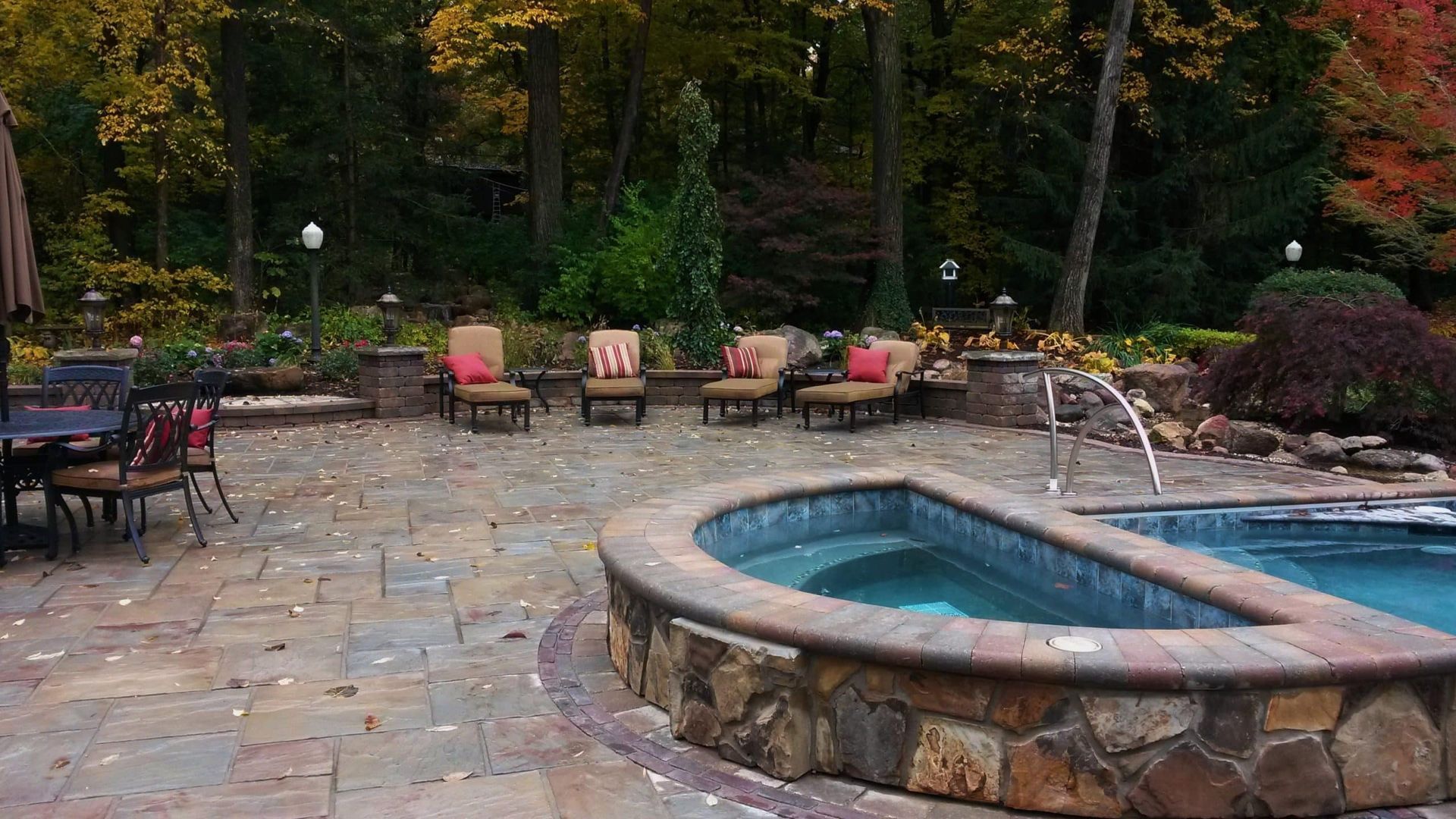 Patio with a hot tub and seating, fall foliage in the background.