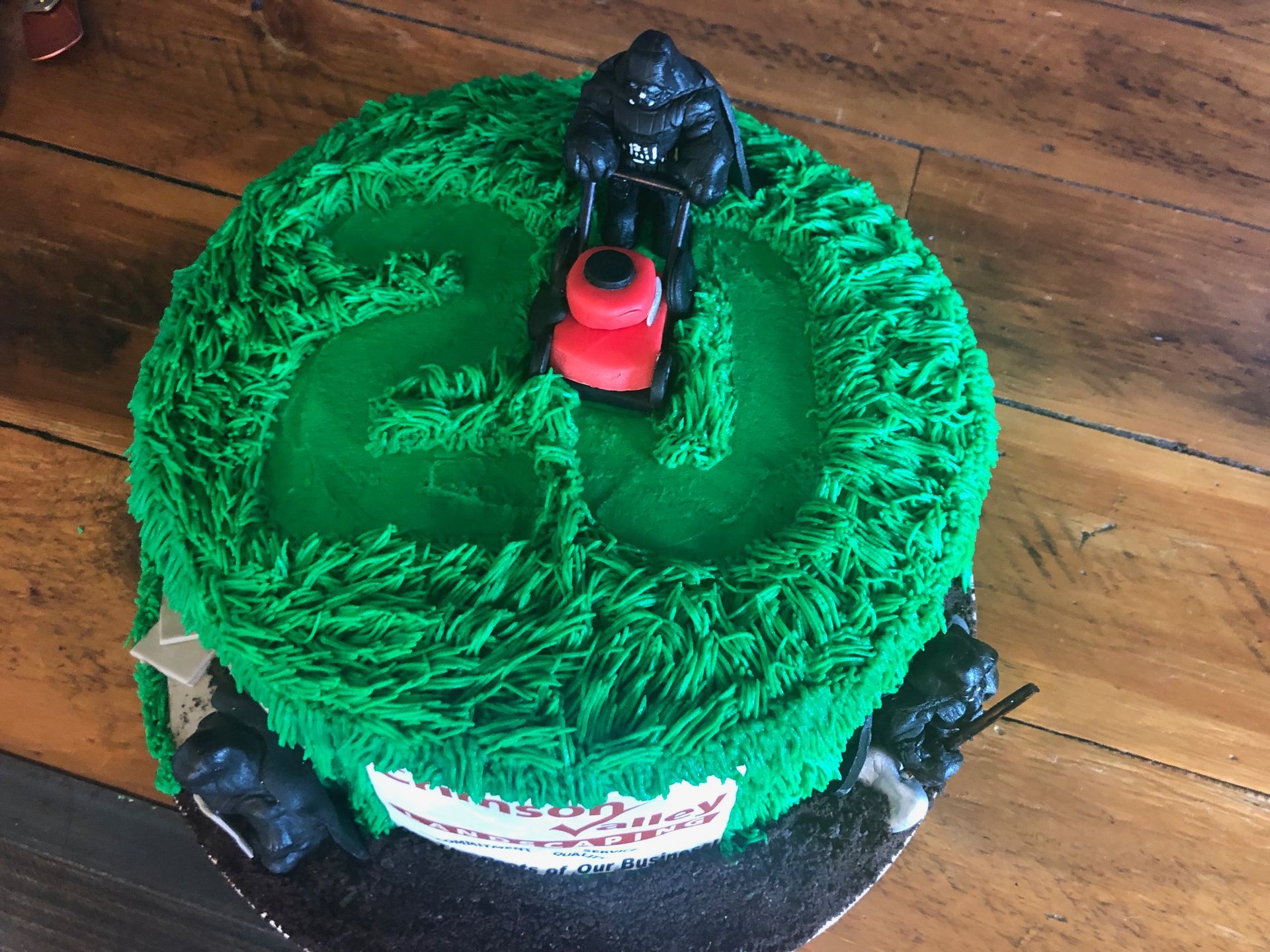 A round, green, grass-textured birthday cake with a black gorilla toy mowing a path; additional gorillas sit at the base.