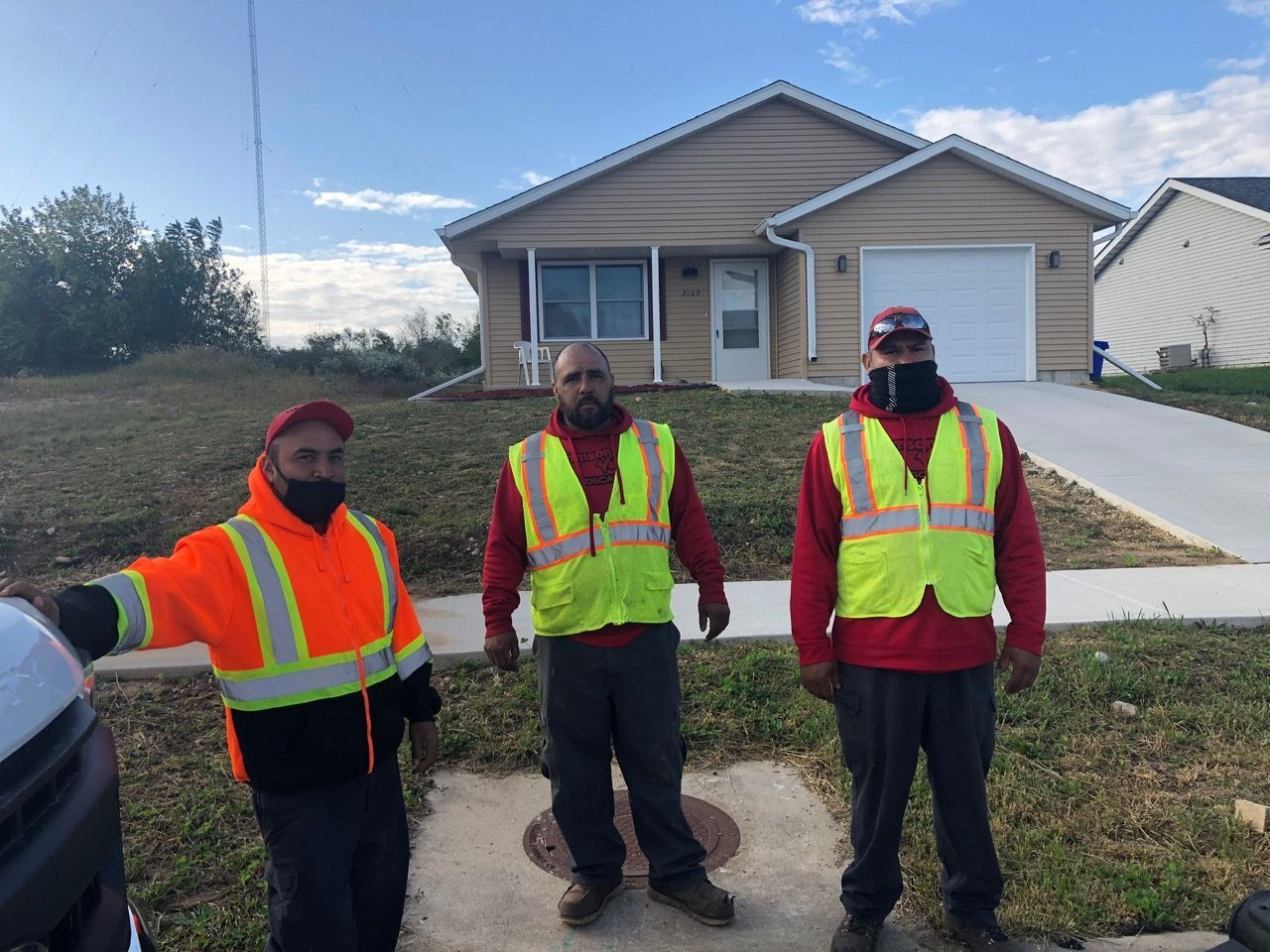 Three workers in high-visibility vests stand outside a suburban house on a sunny day.
