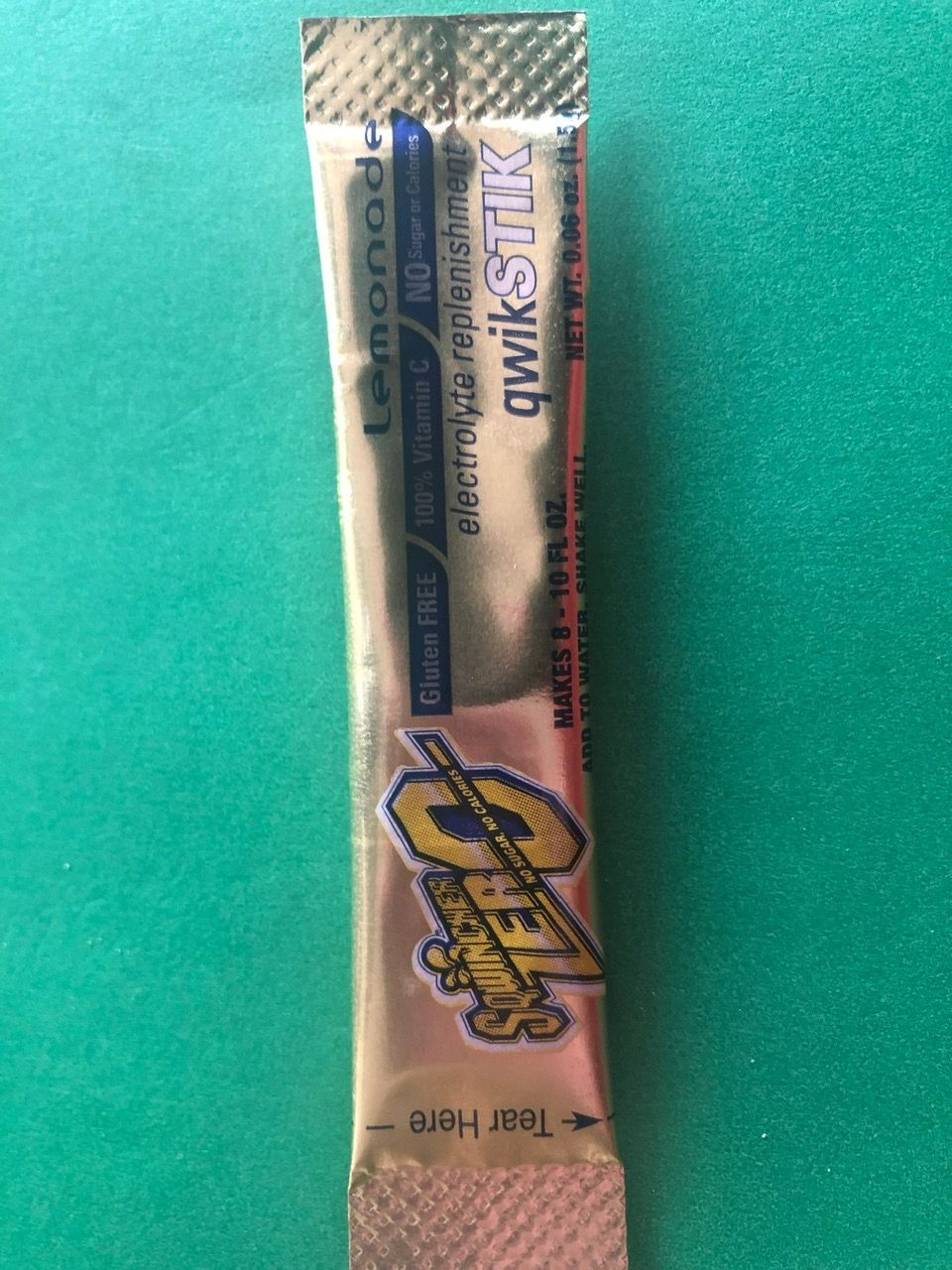 A silver Qwik Stik drink mix packet for Lemonade flavor, placed on a green background.