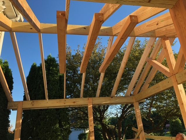 Wooden framework of a building's roof under construction against a clear blue sky.