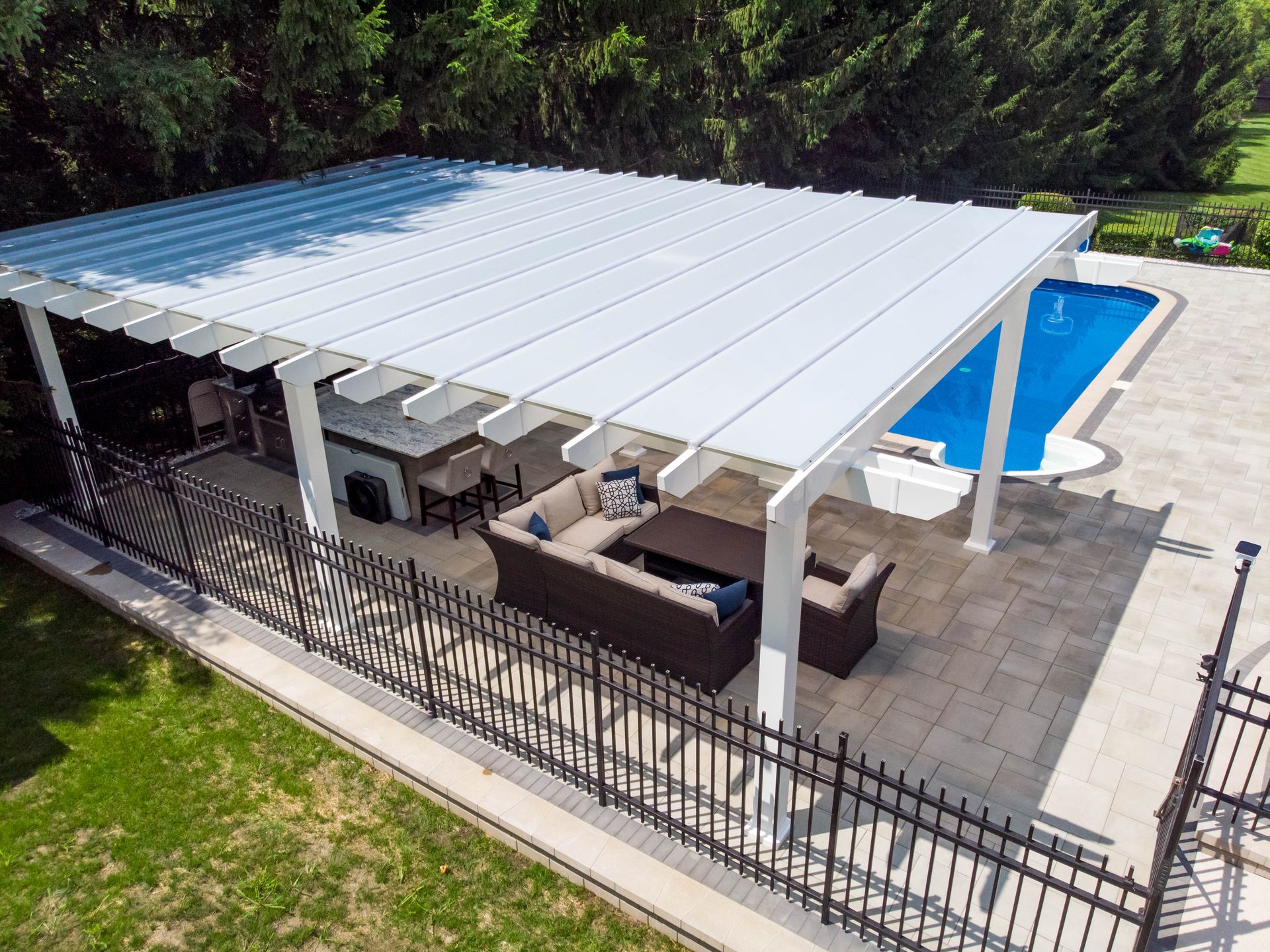 A backyard patio with a white pergola over a seating area and bar, adjacent to an inground swimming pool.