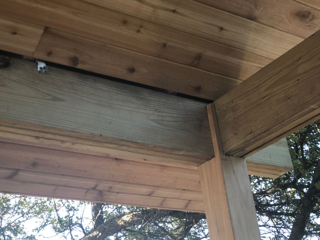 Close-up of wooden structural beams meeting at a post supporting an outdoor roof structure.