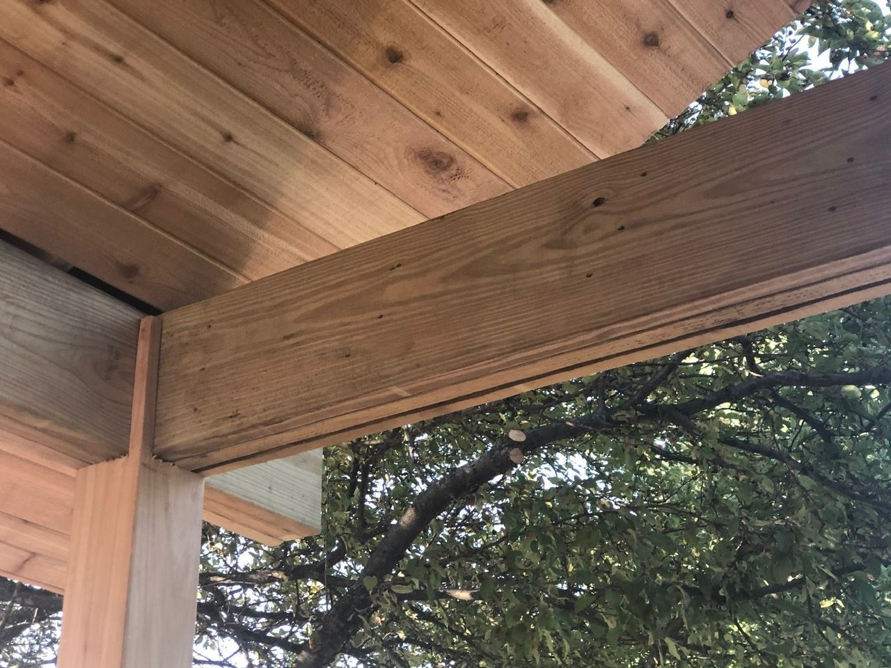 A close-up view of wooden rafters and a support beam under an outdoor roof structure.