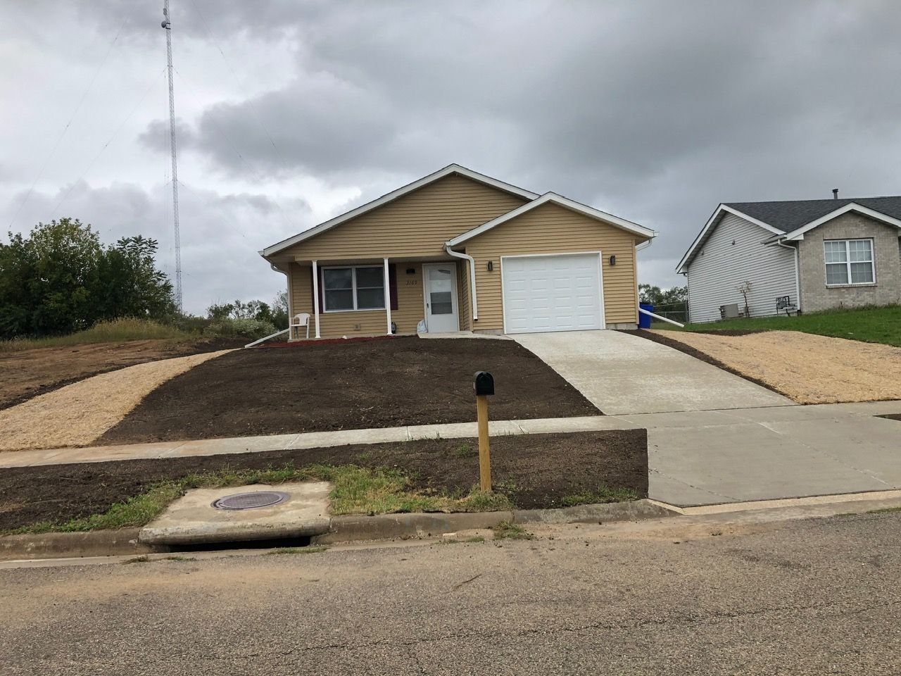 A single-story tan house with a garage and a freshly landscaped yard with gravel borders under a cloudy sky.