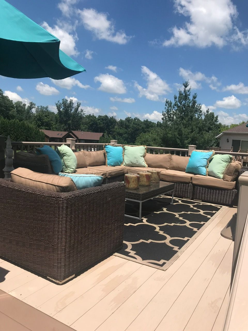 Wicker sectional patio furniture with tan cushions and turquoise pillows on a deck with a black and white geometric rug.