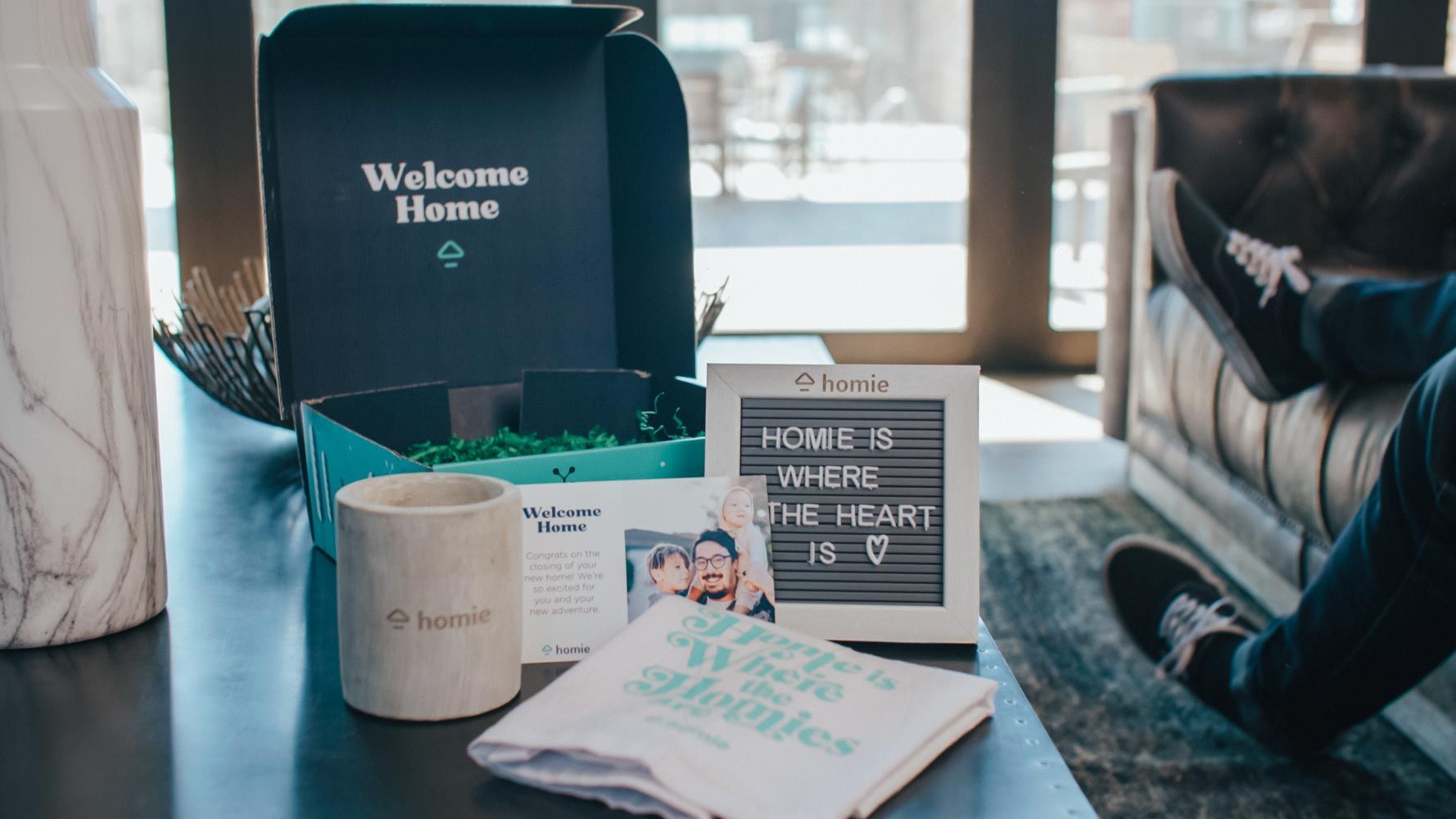 A person is sitting on a couch next to a table with a box and a sign on it.