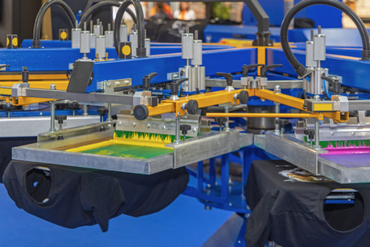 A machine is printing t-shirts on a blue table.