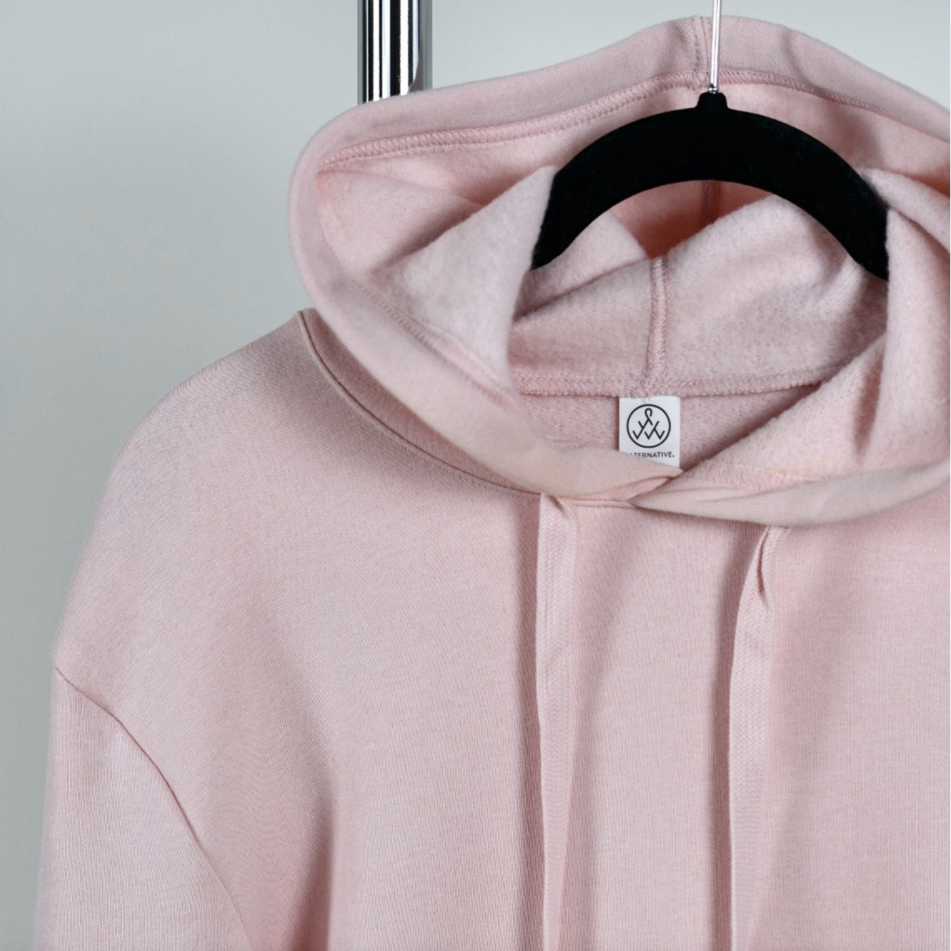 A pink hoodie is hanging on a black hanger