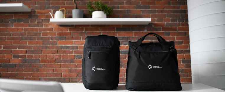 Two black bags are sitting on a desk in front of a brick wall.