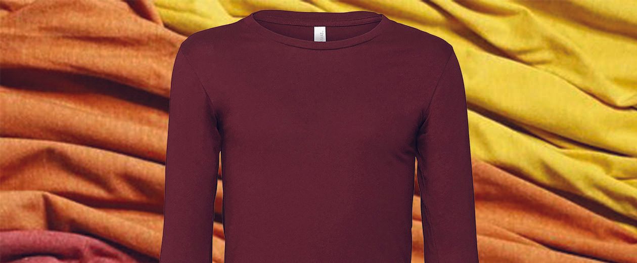 A purple long sleeve t-shirt is sitting on top of a yellow and orange cloth.