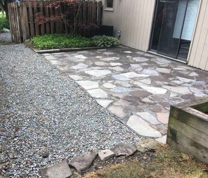 A backyard patio with irregular stone pavers beside a gravel walkway and a small garden area next to a house.