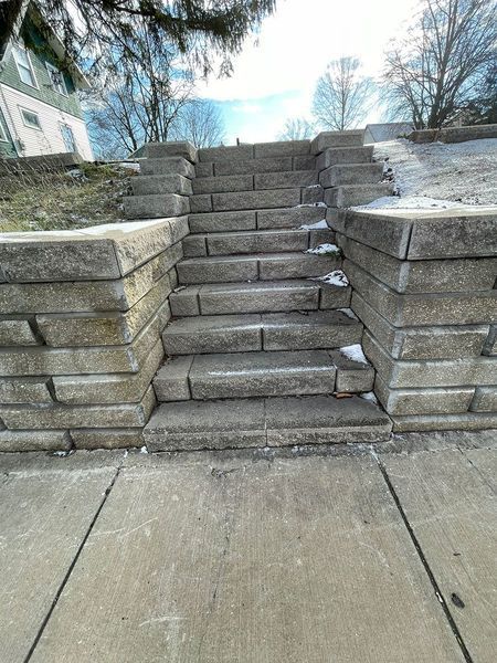 A set of stone stairs leading up to a higher ground level, flanked by stone retaining walls, with patches of snow.