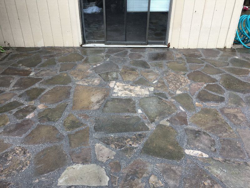 A patio with dark, irregularly shaped flagstones set in gray mortar outside a glass sliding door and beige siding wall.