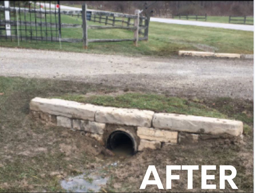 A culvert entrance reinforced with stacked stone blocks set at the edge of a gravel driveway.