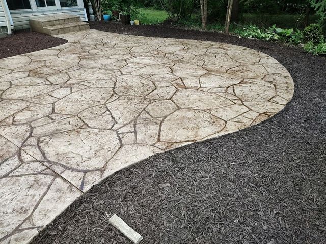 Stamped concrete patio with a stone pattern in beige and brown tones, bordered by dark brown mulch.
