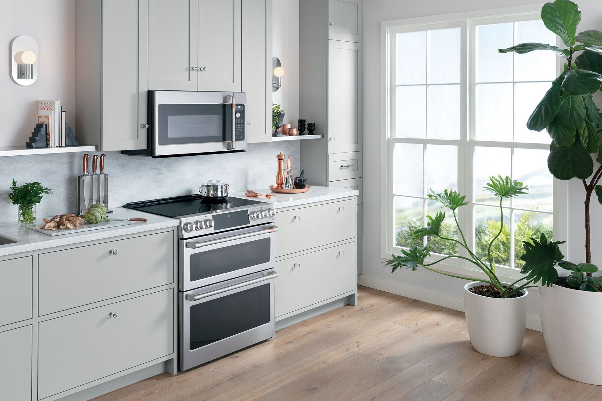 A kitchen with white cabinets , a stove , a microwave , and a window.