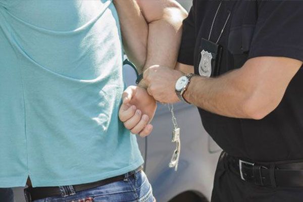 A police officer handcuffs a person wearing a turquoise shirt and jeans.