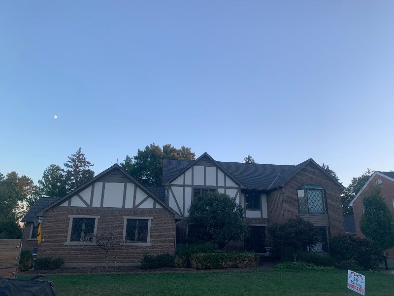 A large brick house with a gray roof and a sign in front of it.